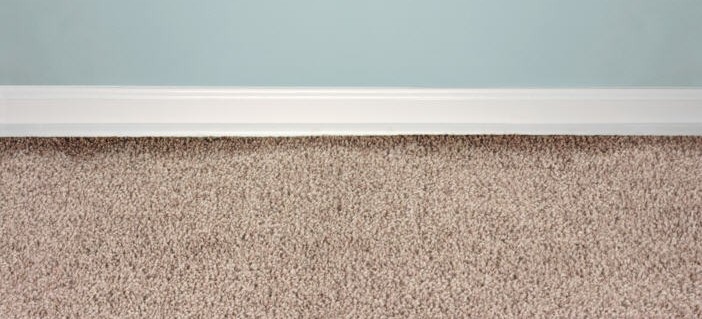 Master Technician using a specialized edge tool to remove dark filtration soiling from carpet baseboards.